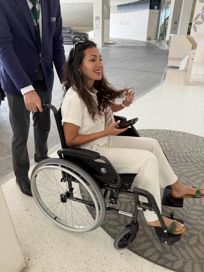 Ma femme en fauteuil roulant devant l'entrée principale de l'hôpital, accompagnée par un agent