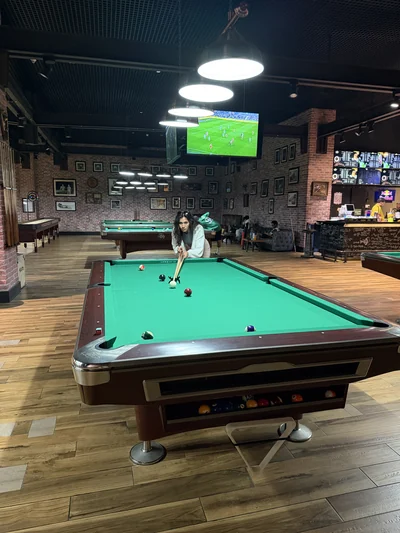 Mon épouse jouant au billard dans un pub, retransmission sportive au fond