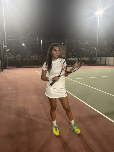 Mon épouse en tenue de tennis blanche sur un court éclairé, la nuit