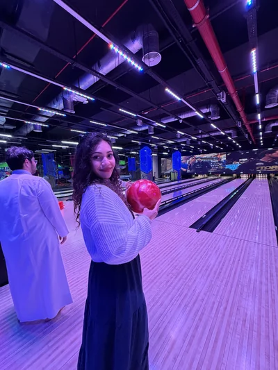 Mon épouse au bowling, boule à la main, devant les pistes éclairées
