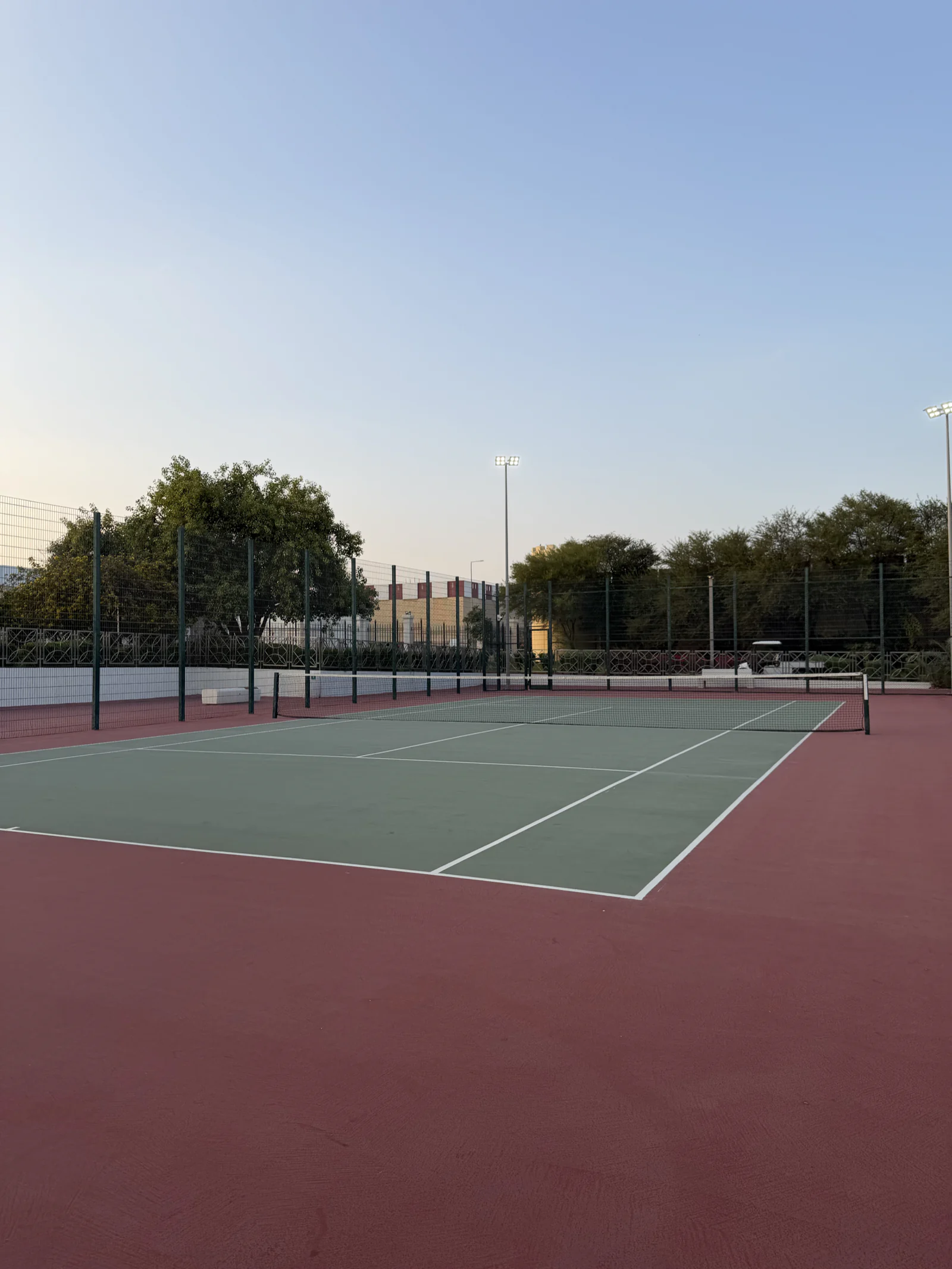 Court de tennis d'Al Bidda Park au crépuscule, entouré d'arbres