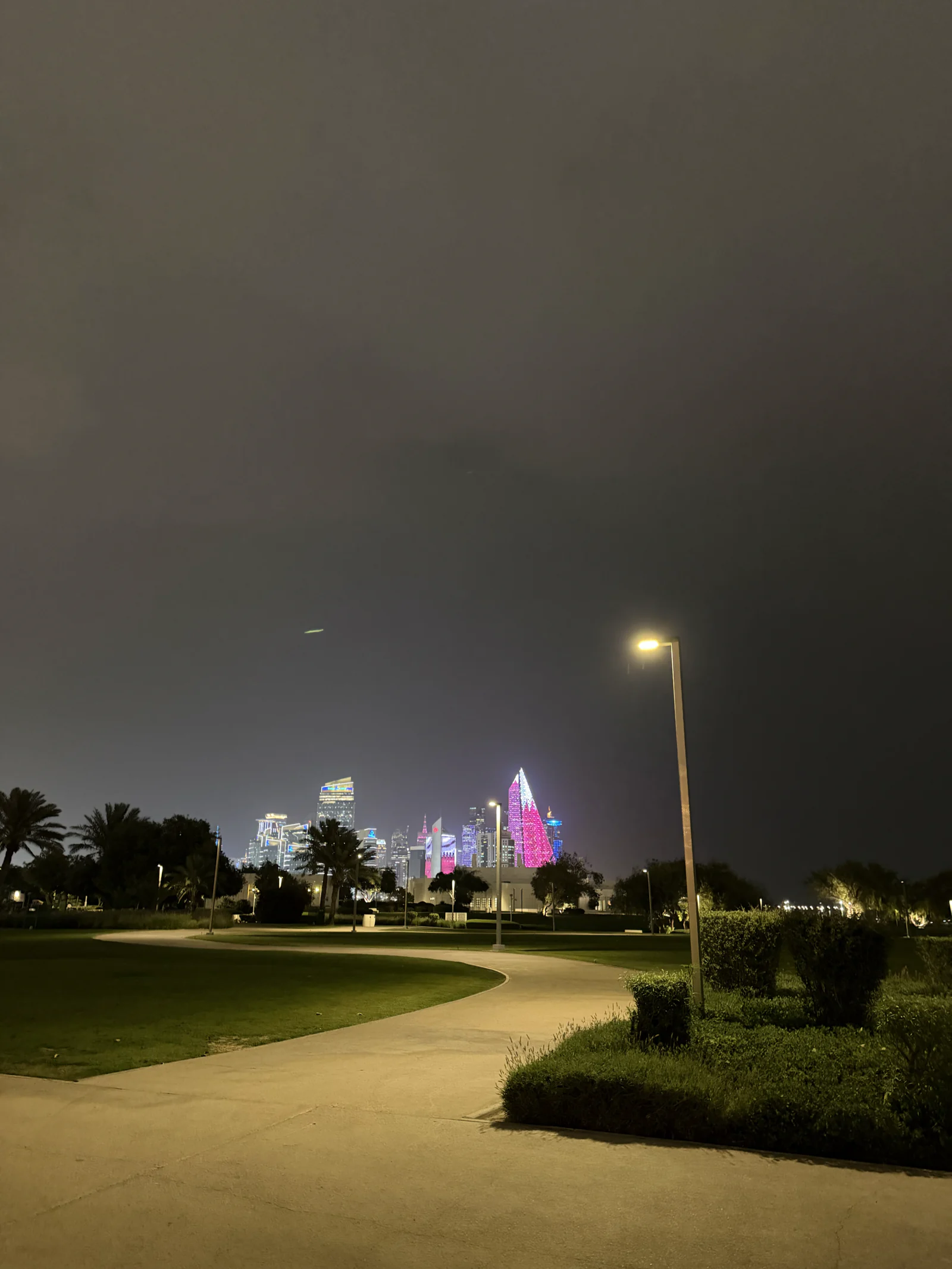 Une allée éclairée d'Al Bidda Park la nuit, les tours de West Bay au loin