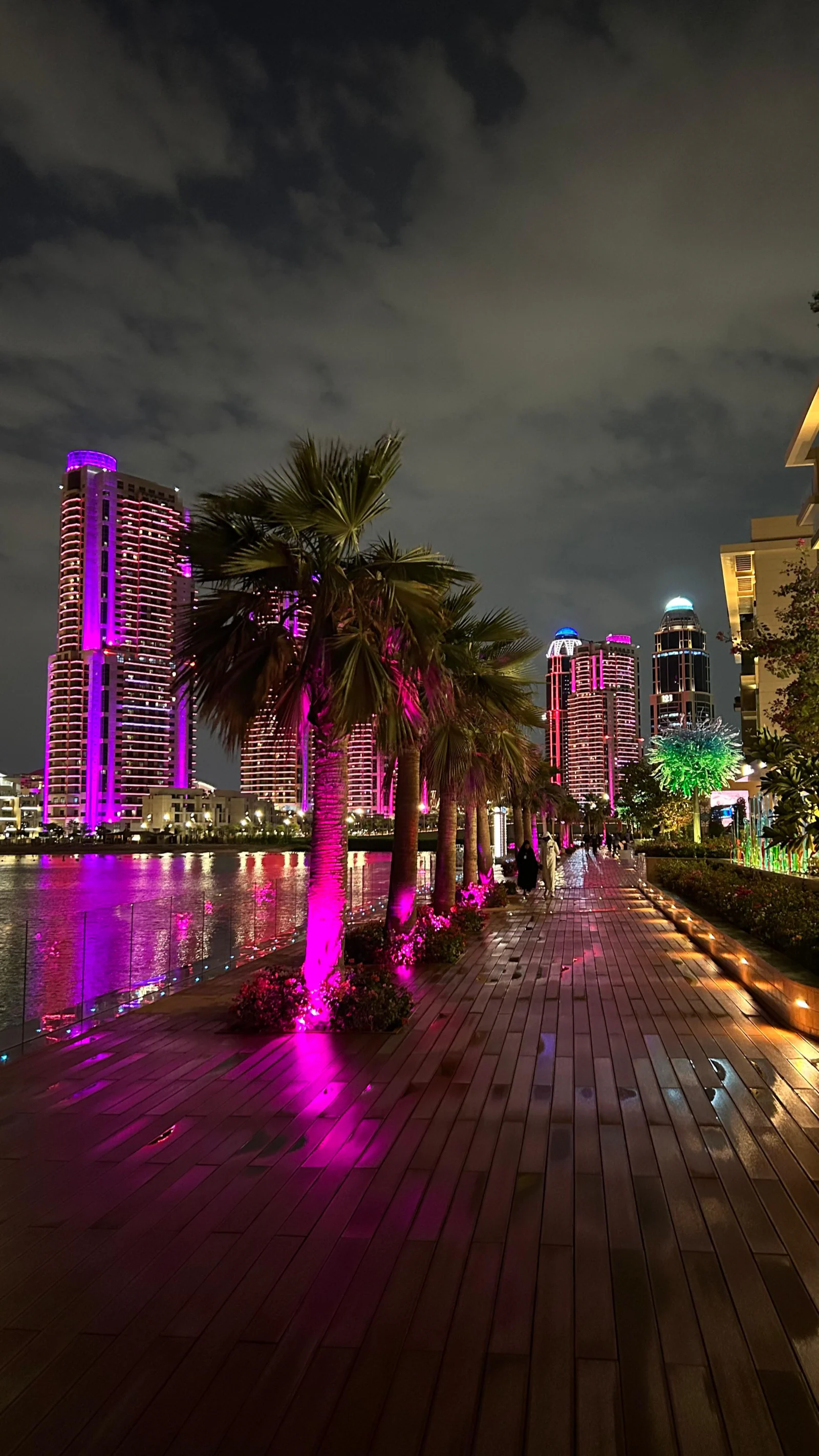 Promenade en bois de Gewan Island la nuit, palmiers éclairés en rose et tours illuminées au fond
