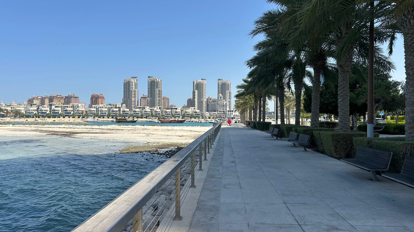 Longue promenade en bord de mer à Lusail, palmiers et immeubles résidentiels au fond