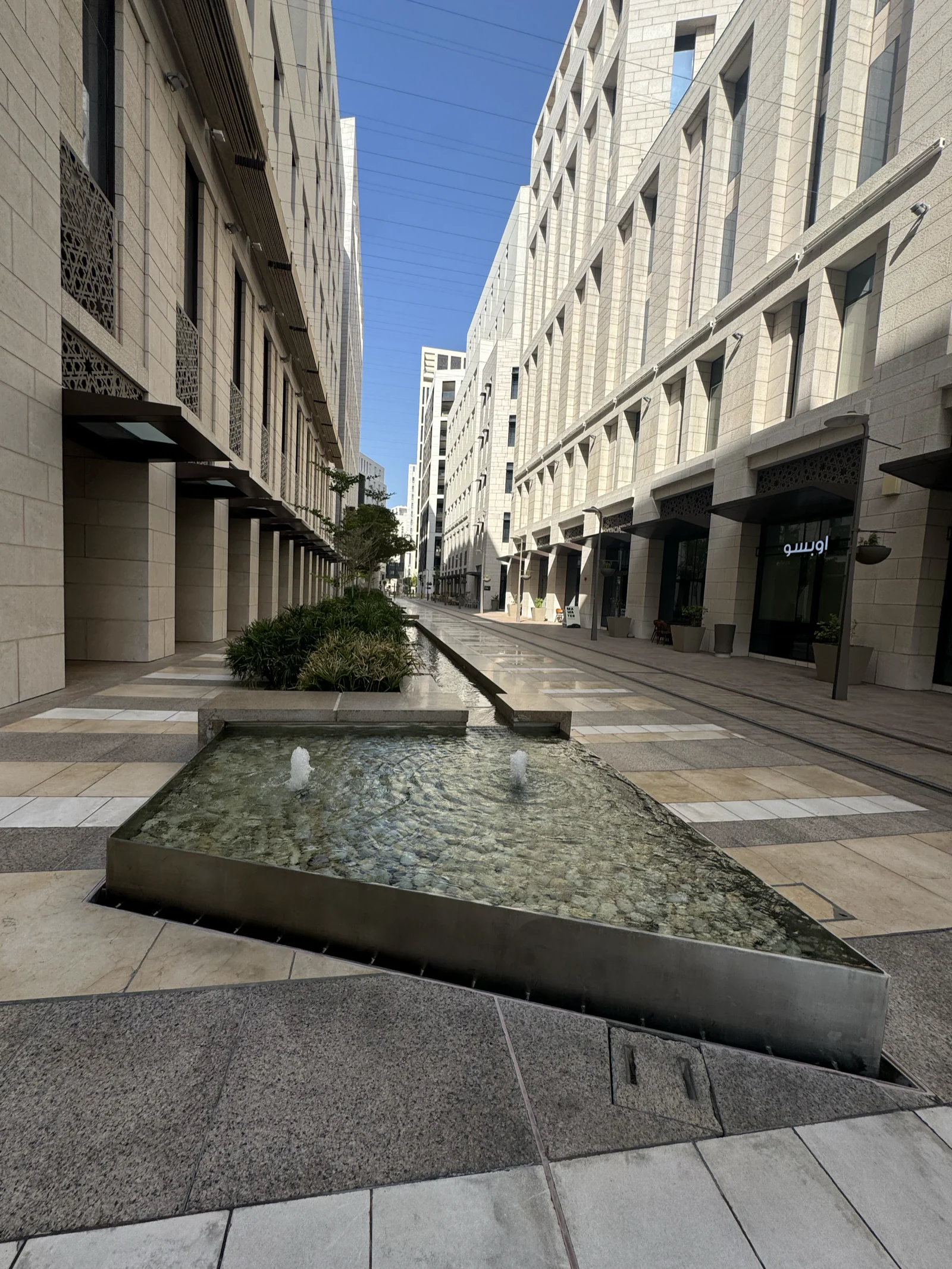 Rue de Msheireb bordée de façades en pierre claire, un long bassin d'eau courante au milieu de la chaussée