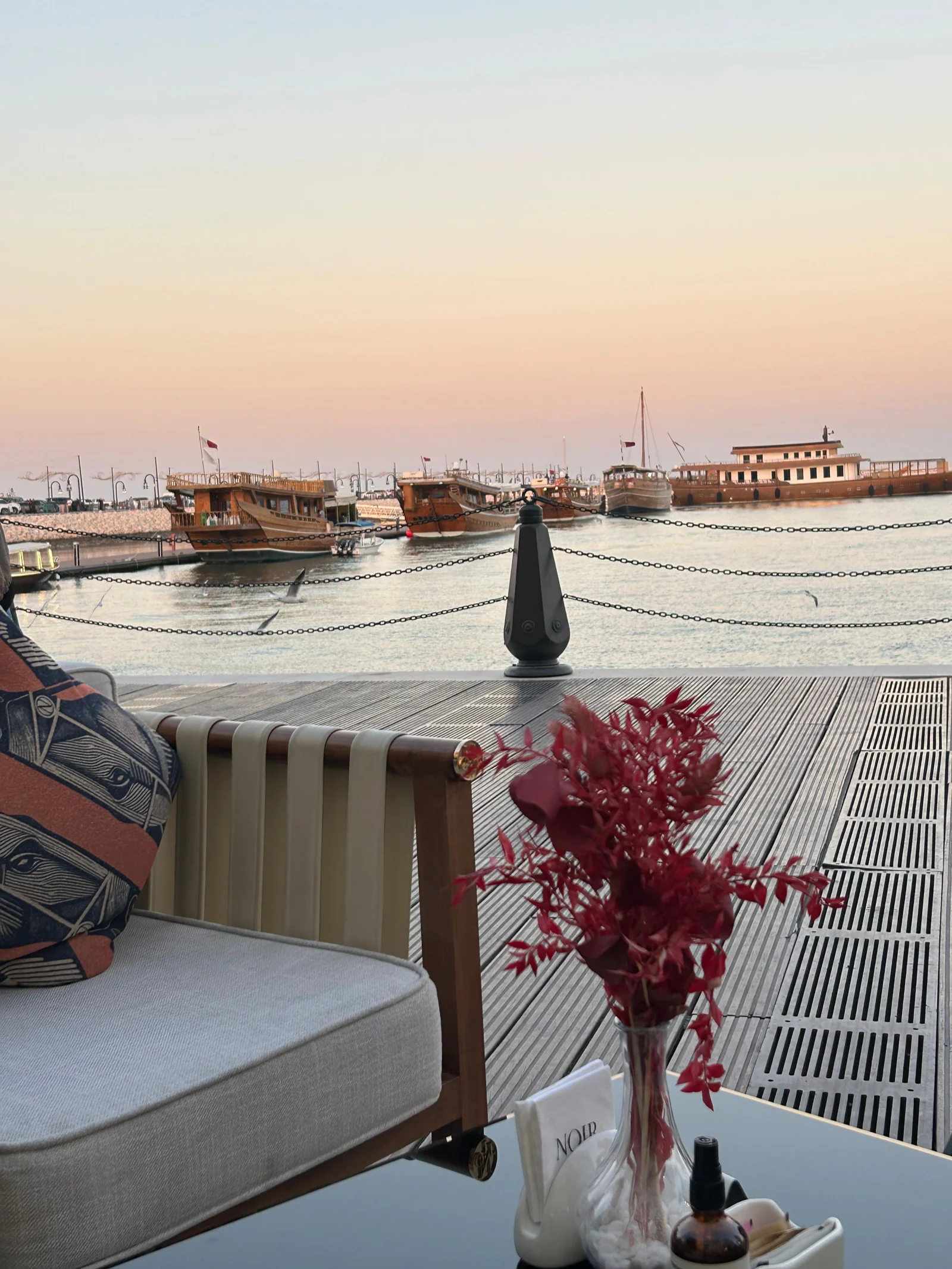 Terrasse en bord d'eau au coucher du soleil, boutres amarrés au vieux port de Doha