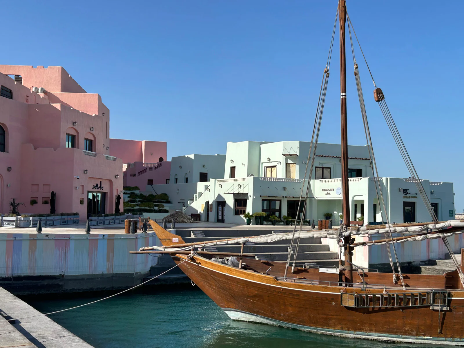 Un boutre traditionnel amarré devant les façades pastel du vieux port de Doha, en plein jour