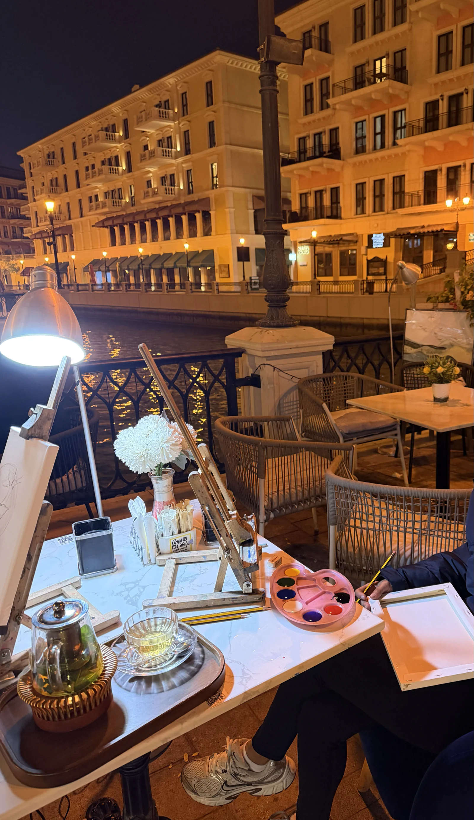 Table de restaurant dressée en terrasse le soir à Qanat Quartier, façades illuminées