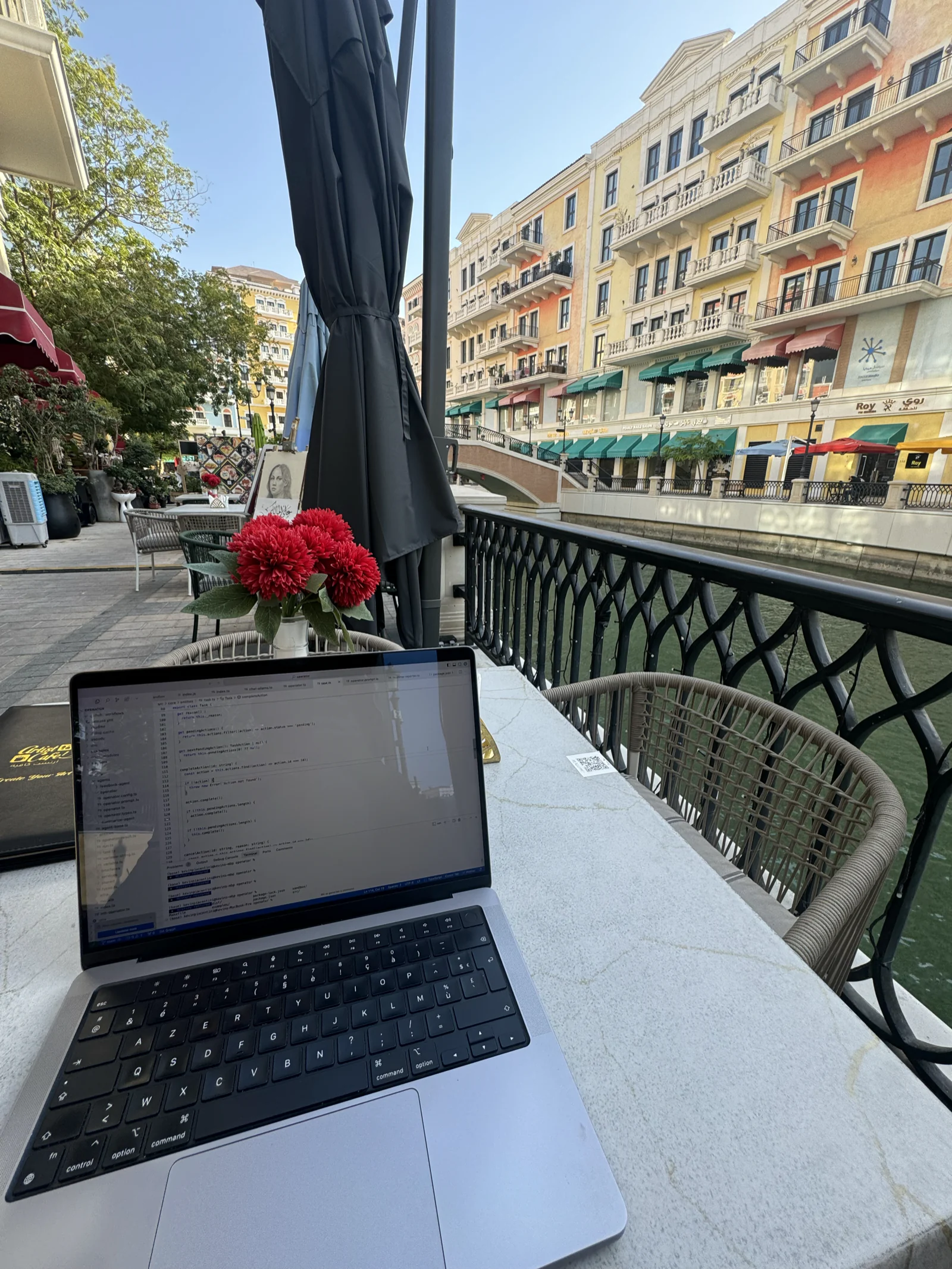 Un ordinateur portable posé sur une table de terrasse donnant sur un canal de Qanat Quartier