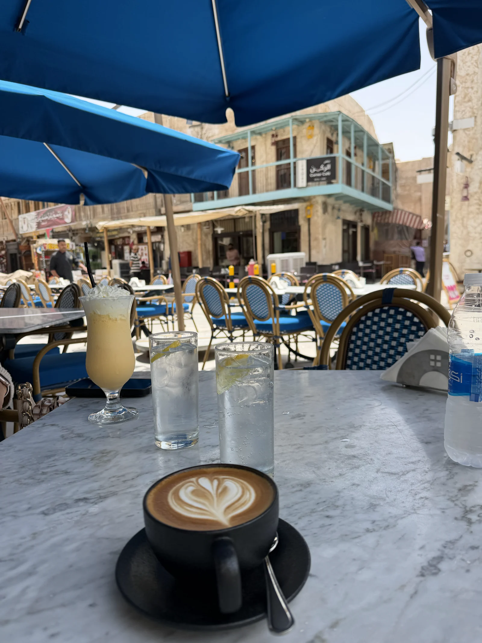 Cappuccino et limonade sur une table de terrasse au souq Waqif, sous un parasol bleu