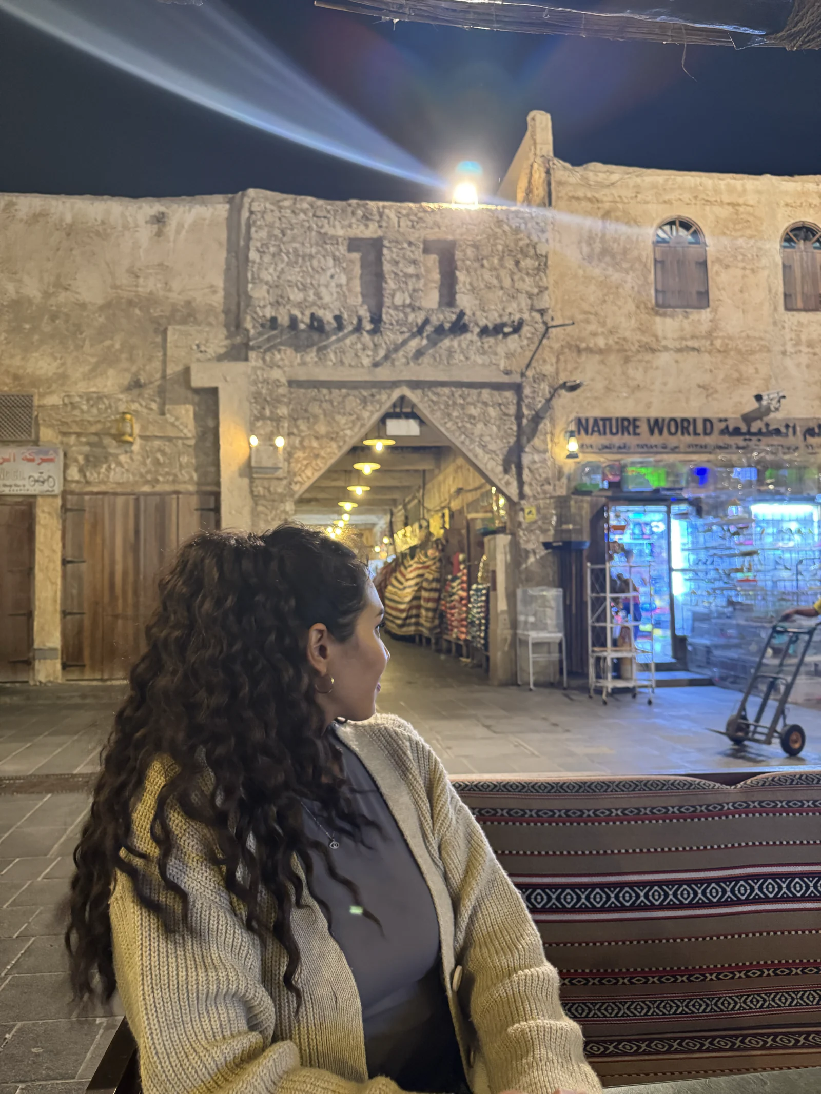 Une visiteuse devant les tapis d'une échoppe du souq Waqif, le soir