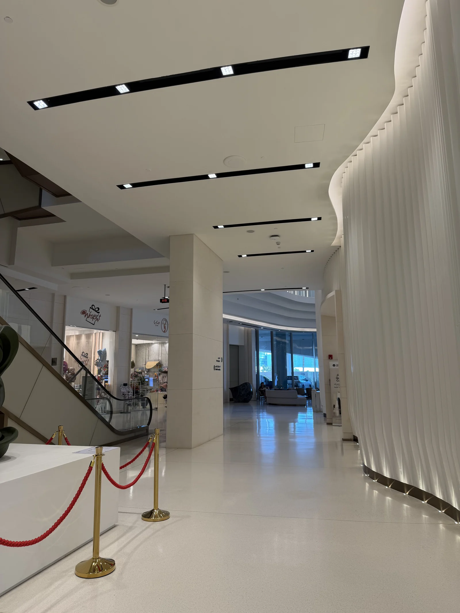 Un hall au mur ondulé, escalier et cordon de velours à l'entrée d'un espace