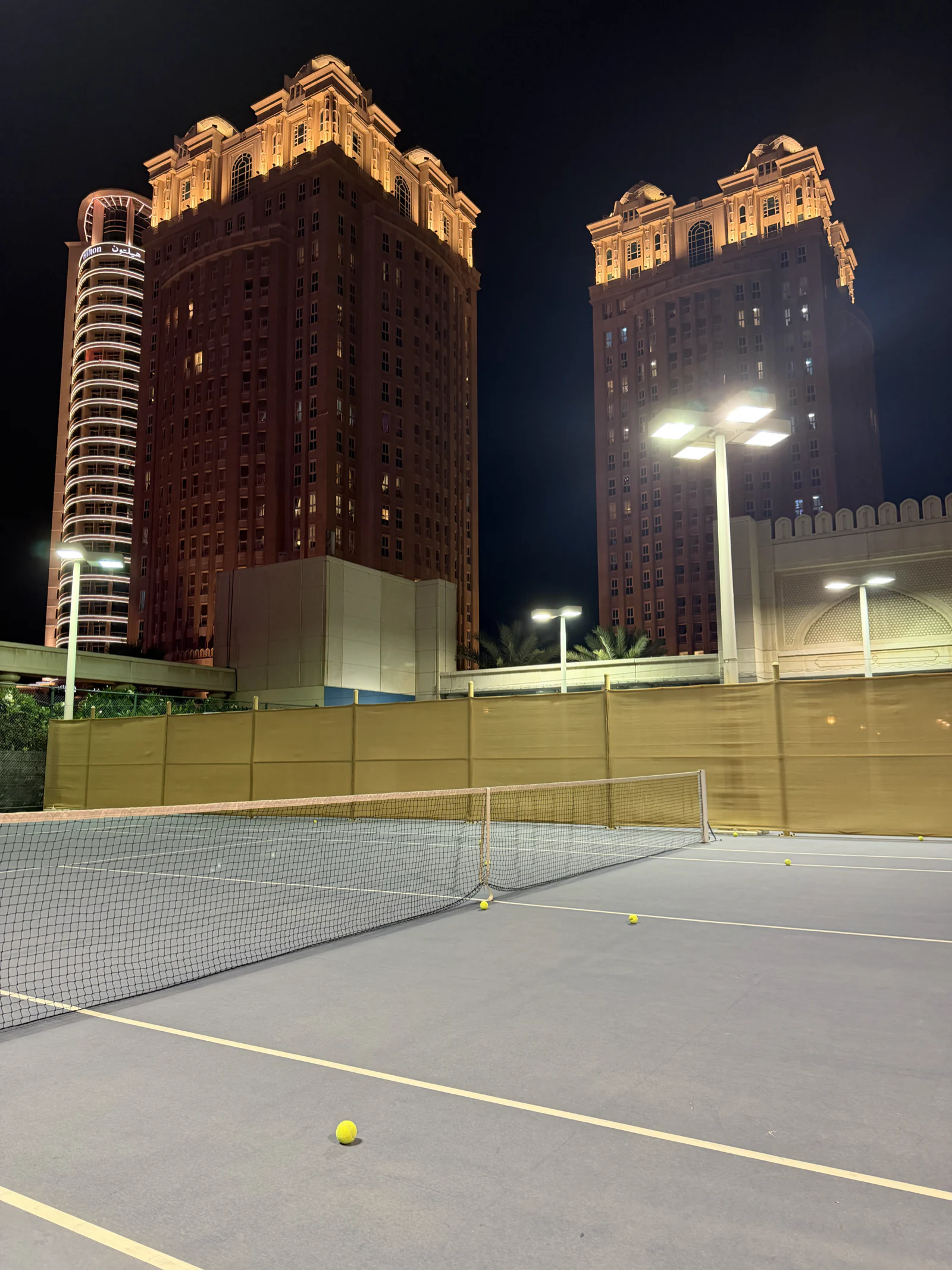 Court de tennis éclairé la nuit au pied des tours de West Bay