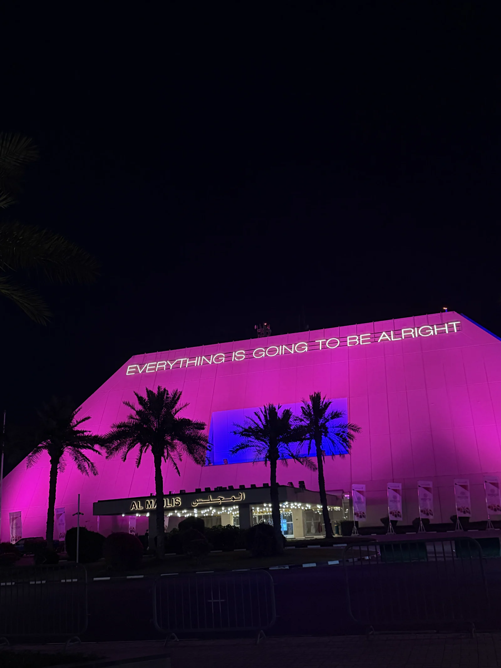 Façade illuminée en rose à West Bay, portant l'inscription lumineuse « Everything is going to be alright »